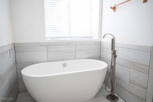 3369 Milenko Dr, Las Vegas, NV 89121 - bathroom featuring tile walls, a freestanding tub, healthy amount of natural light, wainscoting, and tile patterned flooring
