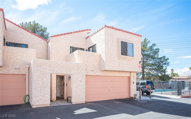 multi unit property featuring a tiled roof, stucco siding, an attached garage, and fence