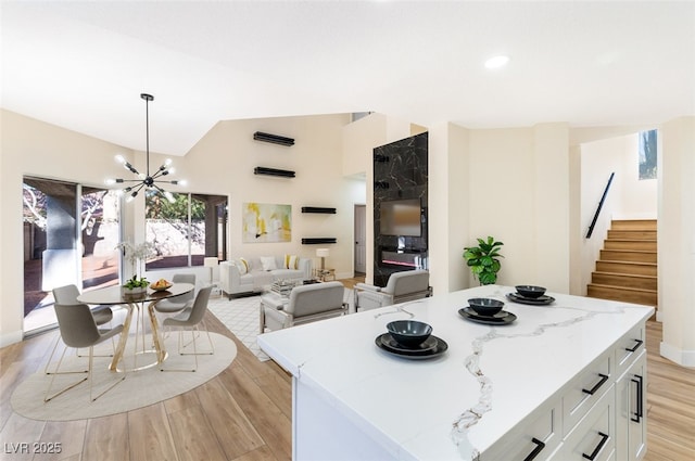 kitchen featuring a notable chandelier, a kitchen island, white cabinetry, light wood-style floors, and lofted ceiling