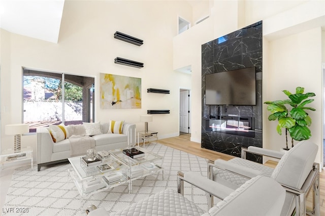 living room with visible vents, baseboards, a fireplace, a high ceiling, and wood finished floors