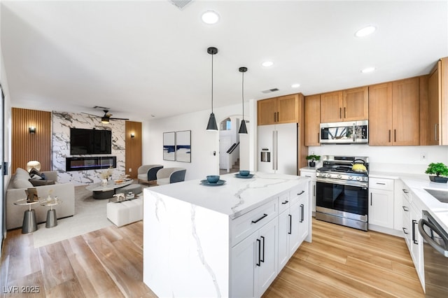 kitchen with a center island, open floor plan, light wood-style flooring, a fireplace, and stainless steel appliances