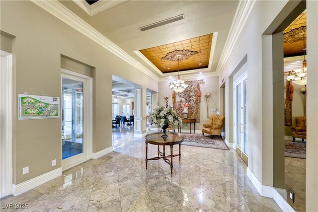 hallway with baseboards, visible vents, an inviting chandelier, a tray ceiling, and ornamental molding