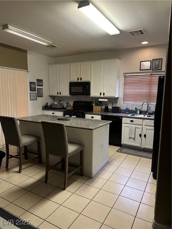 kitchen featuring visible vents, light tile patterned floors, white cabinets, black appliances, and a sink