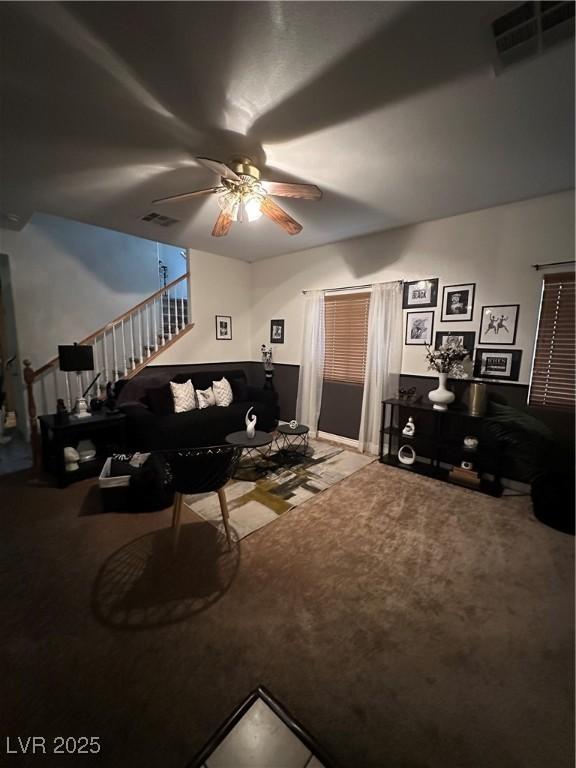 carpeted living room with visible vents, stairs, and ceiling fan