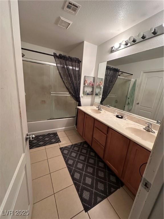 full bath with tile patterned flooring, visible vents, bath / shower combo with glass door, double vanity, and a sink