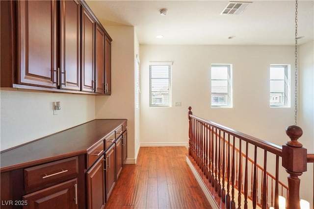 hallway featuring visible vents, baseboards, recessed lighting, dark wood-style flooring, and an upstairs landing