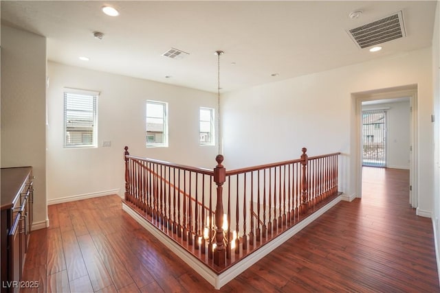 corridor featuring dark wood-type flooring, an upstairs landing, visible vents, and a wealth of natural light