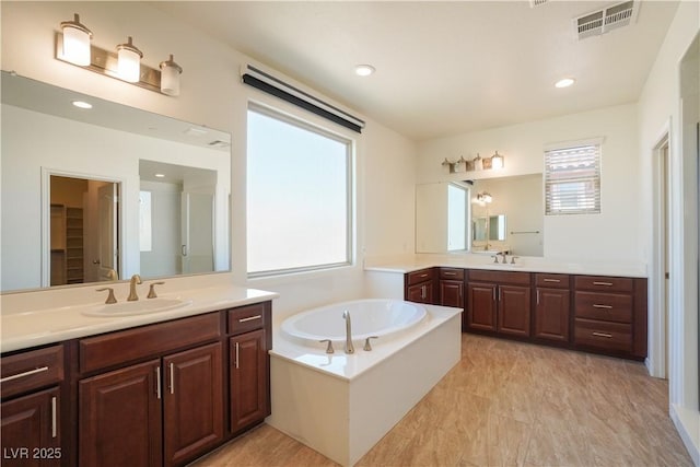 bathroom with two vanities, a bath, visible vents, and a sink