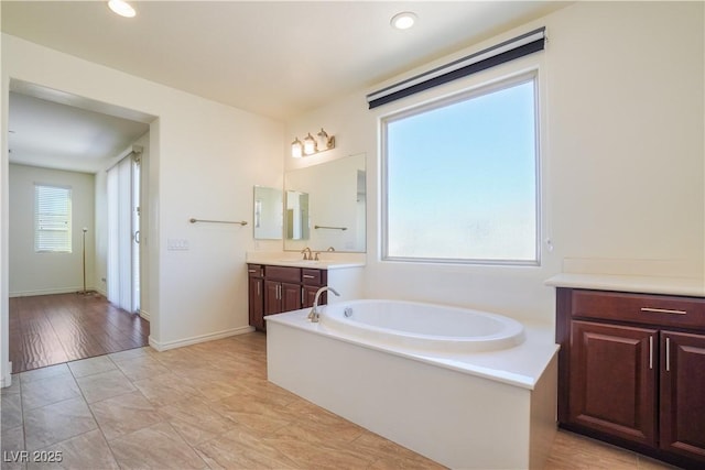 bathroom with baseboards, recessed lighting, vanity, and a garden tub