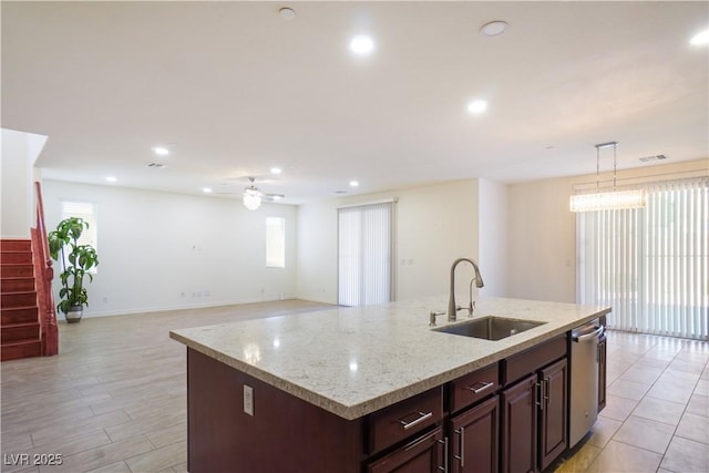 kitchen with a sink, light stone countertops, recessed lighting, hanging light fixtures, and a kitchen island with sink