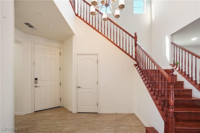 entryway with wood finished floors, visible vents, baseboards, a high ceiling, and a chandelier