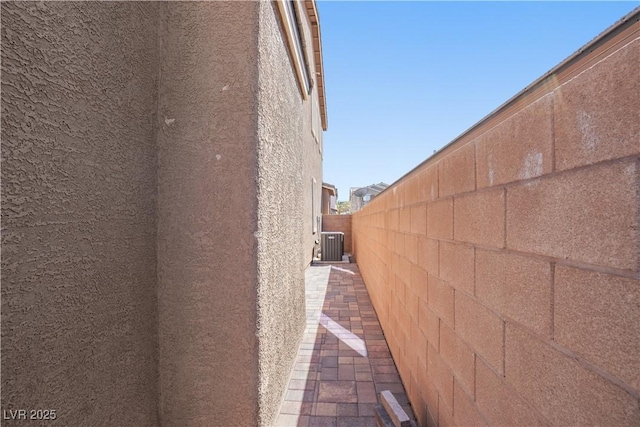 view of side of home with stucco siding, cooling unit, a fenced backyard, and a patio area