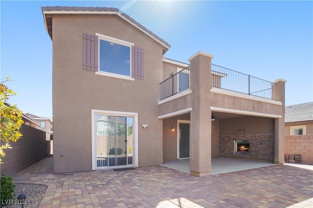 back of house with a patio, stucco siding, fence, and a lit fireplace