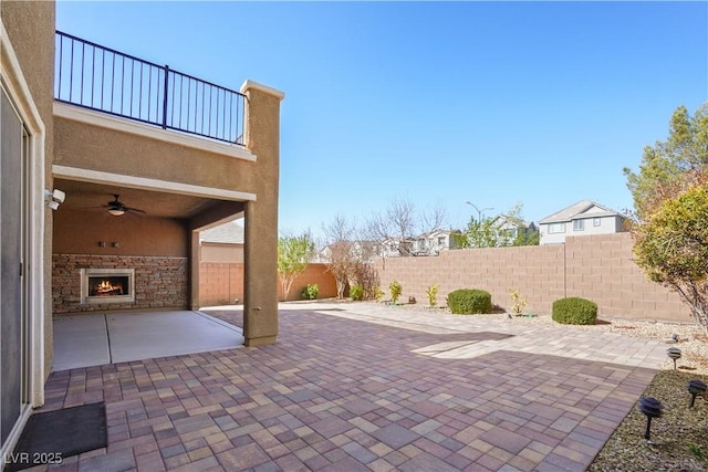 view of patio featuring an outdoor stone fireplace, a fenced backyard, and ceiling fan