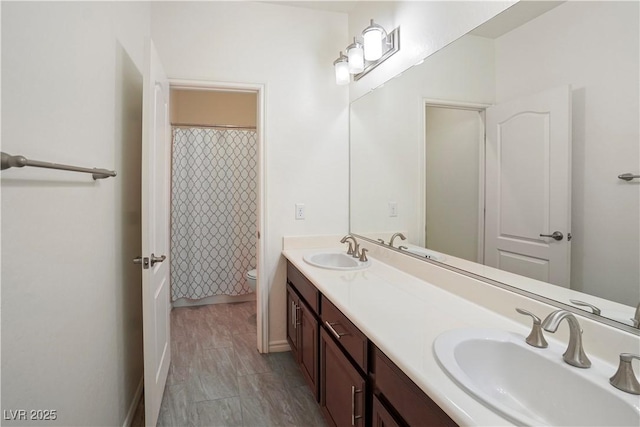 bathroom featuring double vanity, toilet, baseboards, and a sink