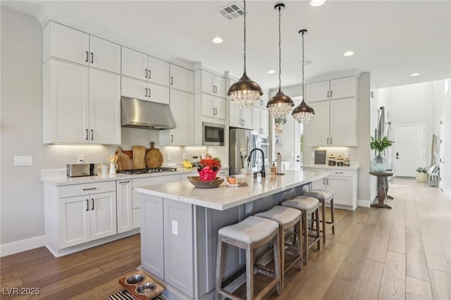 kitchen with visible vents, hardwood / wood-style flooring, under cabinet range hood, appliances with stainless steel finishes, and light countertops