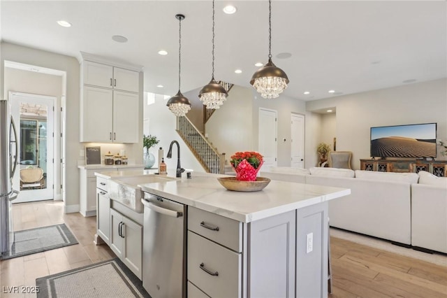 kitchen with open floor plan, an island with sink, light wood-type flooring, stainless steel appliances, and a sink