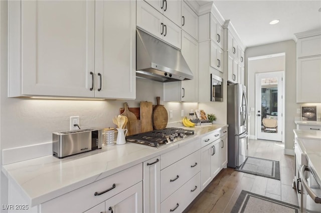 kitchen with light stone counters, wood finished floors, stainless steel appliances, under cabinet range hood, and white cabinetry