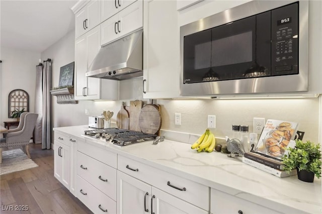 kitchen with under cabinet range hood, light stone counters, dark wood finished floors, appliances with stainless steel finishes, and white cabinets