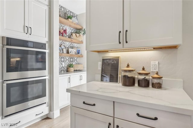 kitchen with open shelves, light stone countertops, double oven, and white cabinets