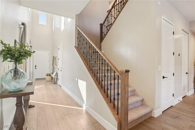 stairway with baseboards, a towering ceiling, and hardwood / wood-style flooring