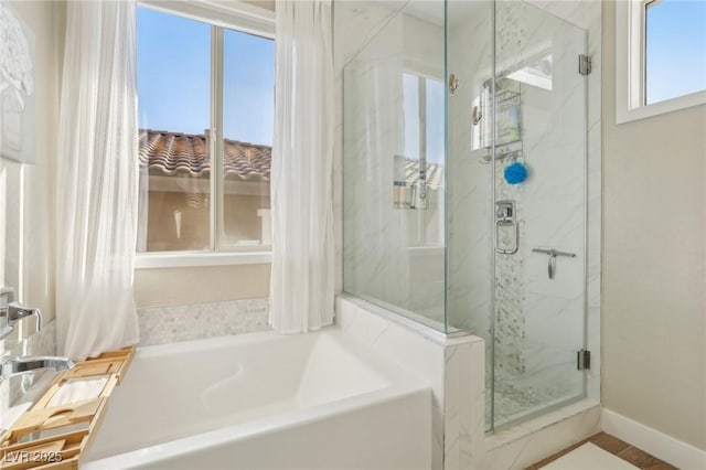 bathroom featuring a marble finish shower, baseboards, and a garden tub