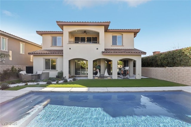 rear view of house featuring a tiled roof, a lawn, stucco siding, a balcony, and a patio area