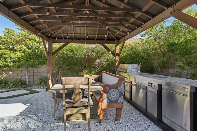 view of patio with outdoor dining space, fence, exterior kitchen, a gazebo, and a grill