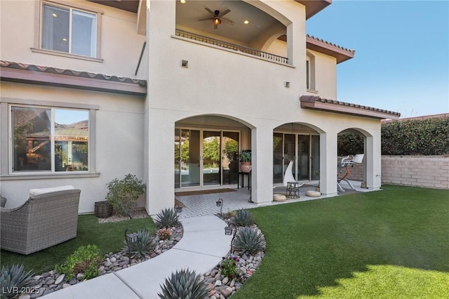 back of property featuring a patio, a balcony, a yard, stucco siding, and a tile roof