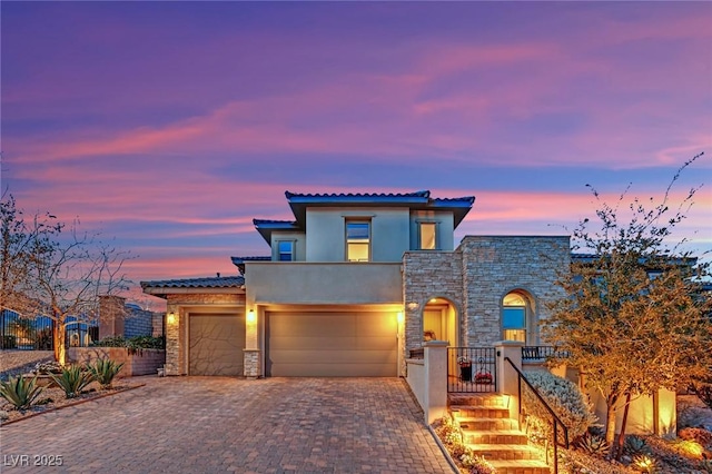 mediterranean / spanish-style house with stucco siding, decorative driveway, stone siding, fence, and a garage