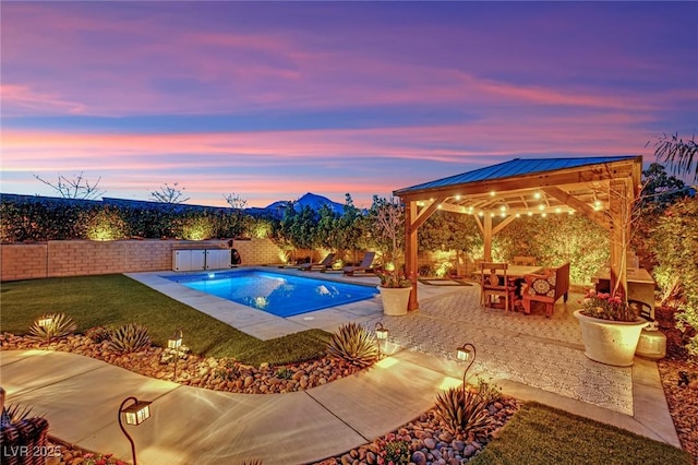 pool at dusk featuring a lawn, a fenced backyard, a gazebo, a fenced in pool, and a patio area