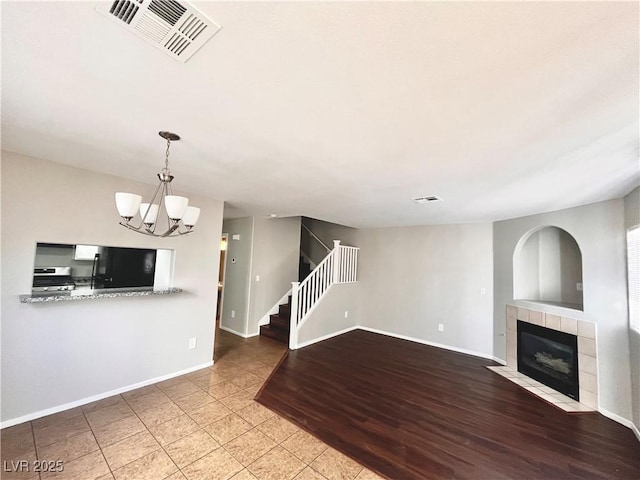 unfurnished living room featuring visible vents, stairway, a fireplace, baseboards, and a chandelier