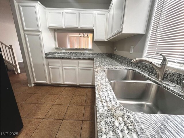 kitchen featuring white cabinets, stone countertops, dark tile patterned flooring, and a sink