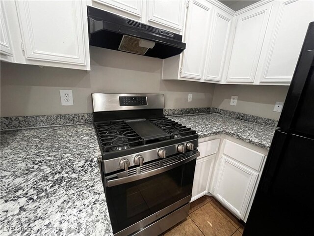 kitchen featuring light stone countertops, under cabinet range hood, stainless steel range with gas stovetop, freestanding refrigerator, and white cabinetry