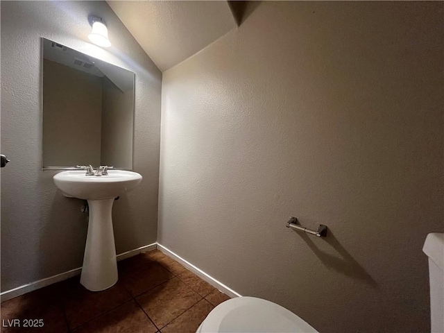 half bathroom with tile patterned floors, baseboards, toilet, and vaulted ceiling