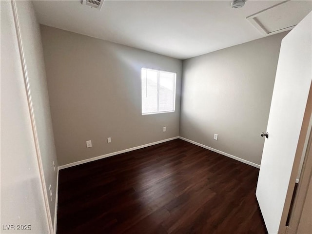 unfurnished room with dark wood finished floors, attic access, visible vents, and baseboards