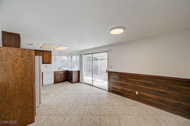 kitchen featuring light countertops, light tile patterned floors, freestanding refrigerator, white dishwasher, and a sink