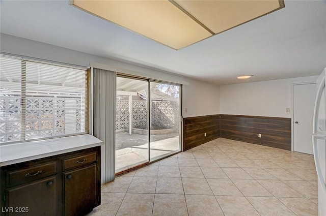 empty room with wooden walls, light tile patterned flooring, and a wainscoted wall