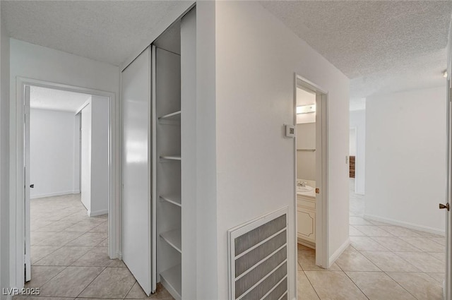 corridor with light tile patterned flooring, a textured ceiling, and baseboards