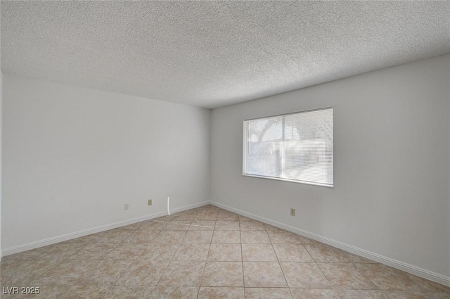 empty room featuring light tile patterned floors, baseboards, and a textured ceiling