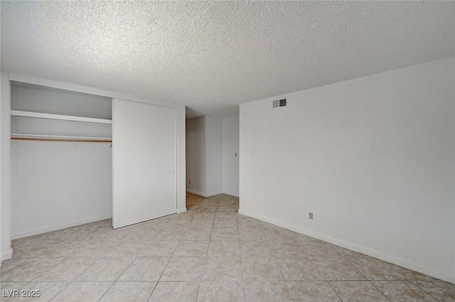 unfurnished bedroom with visible vents, a textured ceiling, a closet, tile patterned flooring, and baseboards