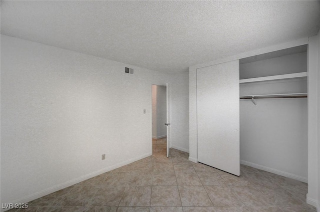 unfurnished bedroom featuring visible vents, a textured ceiling, a closet, light tile patterned flooring, and baseboards