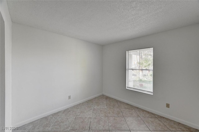 spare room featuring light tile patterned floors, baseboards, and a textured ceiling