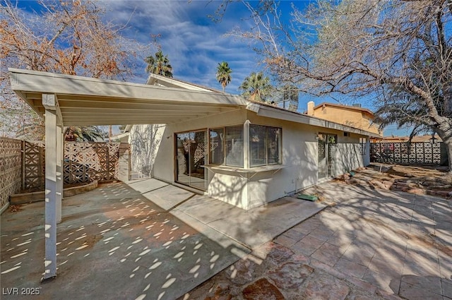 rear view of house with stucco siding, a patio, a carport, and fence private yard