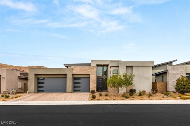 contemporary home with stucco siding, an attached garage, and decorative driveway
