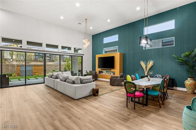 living area with an accent wall, baseboards, recessed lighting, a towering ceiling, and wood finished floors