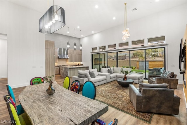 living room with light wood-type flooring, baseboards, visible vents, and a towering ceiling