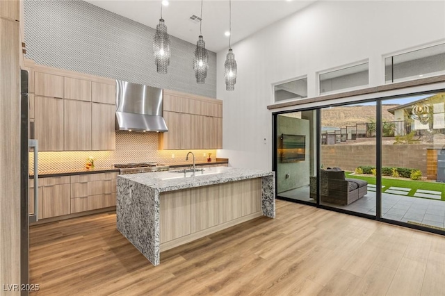 kitchen with wall chimney range hood, modern cabinets, light wood-style floors, and light brown cabinetry