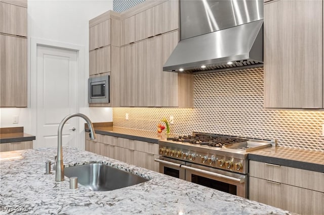 kitchen with light brown cabinets, wall chimney range hood, appliances with stainless steel finishes, modern cabinets, and a sink