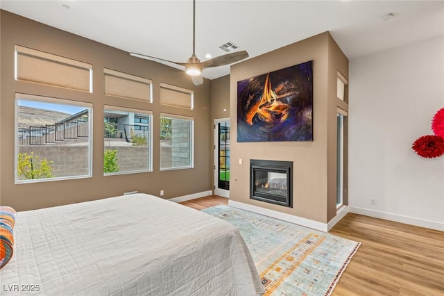 bedroom with a glass covered fireplace, wood finished floors, and baseboards